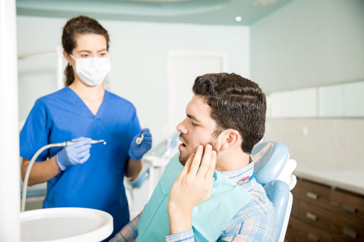 Man in a dental chair holding his jaw after a knocked-out tooth