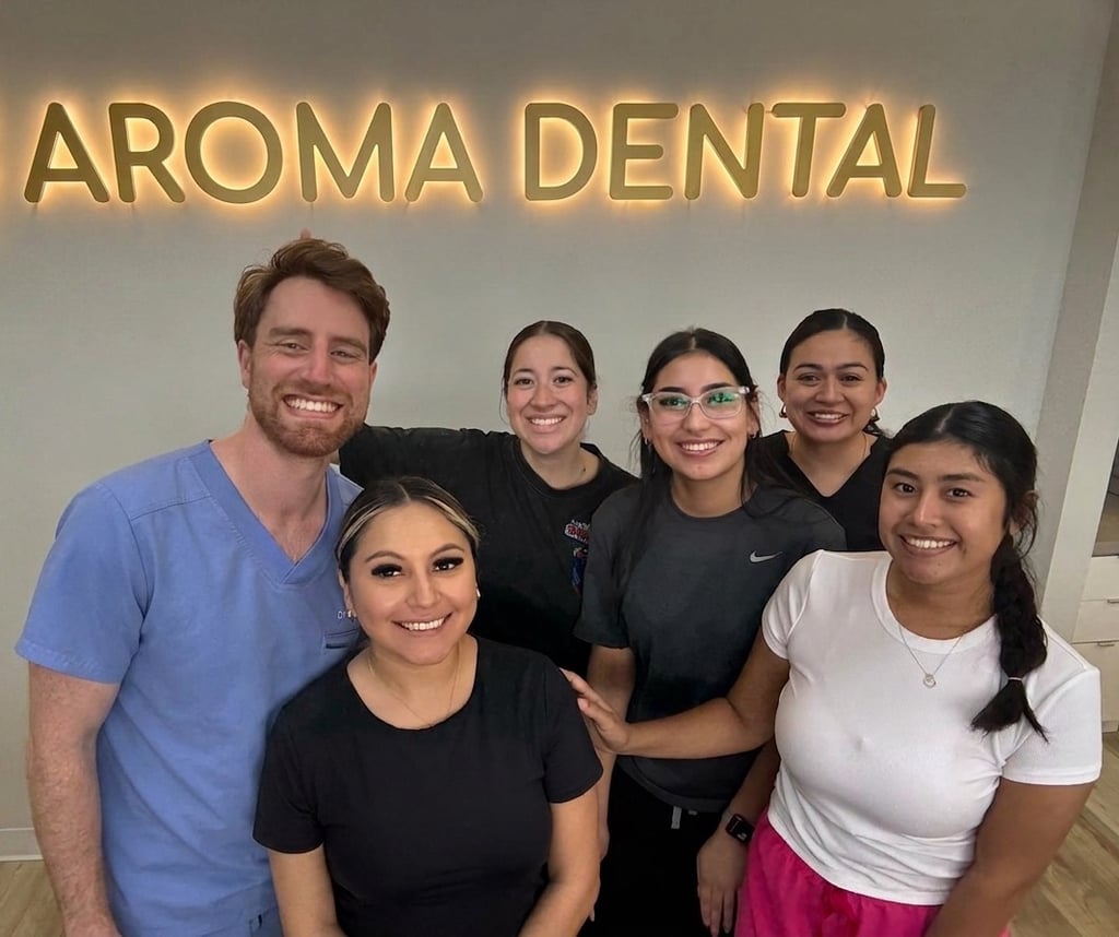 Aroma Dental team smiling in front of the illuminated clinic sign
