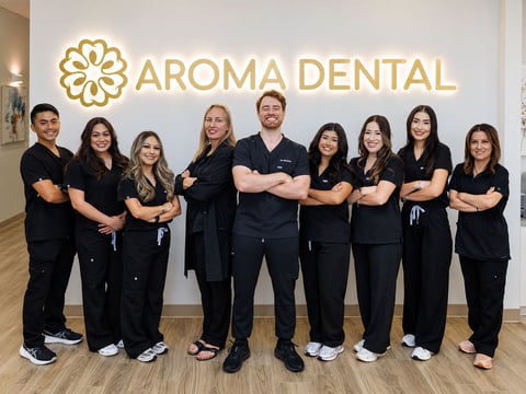The full Aroma Dental team standing together in front of the Aroma Dental logo wall